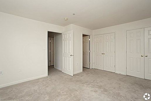 Carpeted bedroom with two double door closets, doors leading to hallway and bathroom